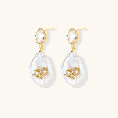Gold-plated drop earrings with iridescent baroque pearls and crystal flower accents on cream background