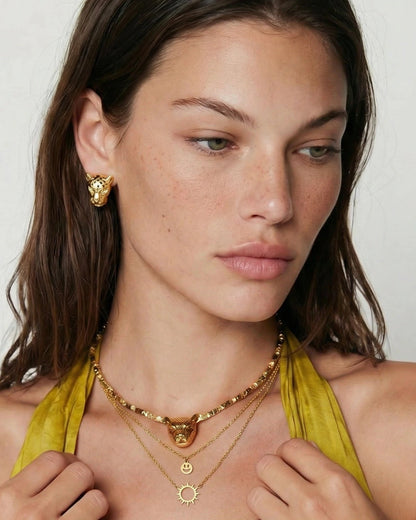 Woman wearing gold jewelry including earrings and necklaces against a plain background